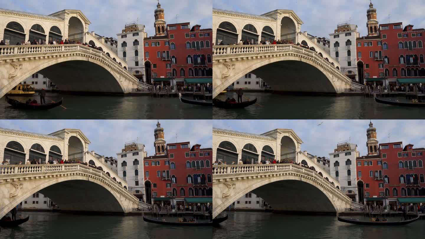 意大利威尼斯历史悠久的里亚托桥上挤满了游客，游客们看到贡多拉传统船只在运河上驶过