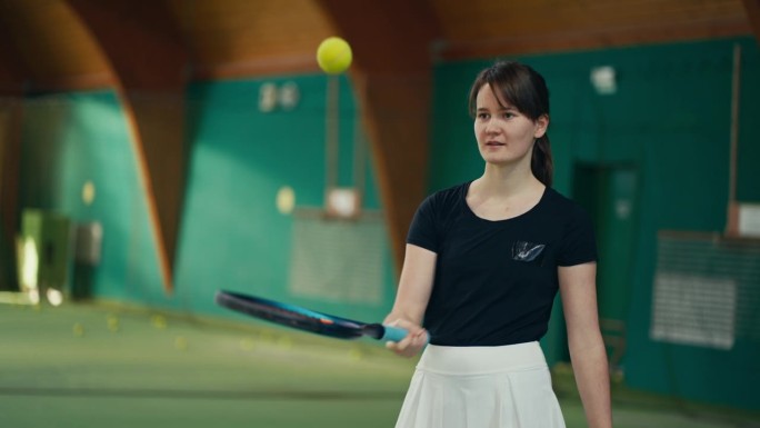 在体育俱乐部的球场上，微笑的年轻女网球运动员在拍子上弹着球