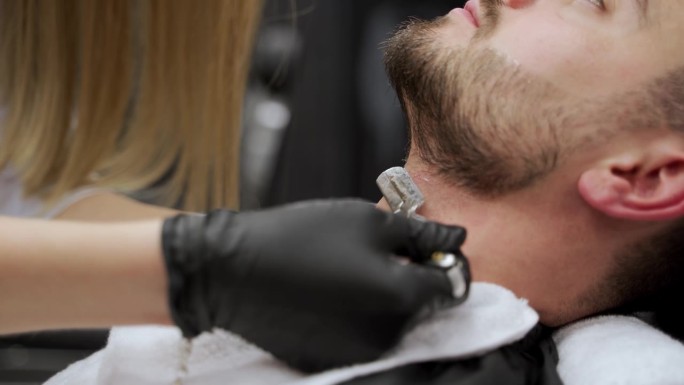 专业女理发师在高档沙龙为男性客户提供精准的胡须修剪服务。专家使用直剃刀，精炼面部毛发，确保修饰舒适，