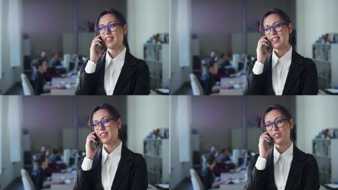 成功的女商人在办公室的肖像，打重要的电话，并与投资者达成协议。在后台使用电脑的公司员工。团队经理使用