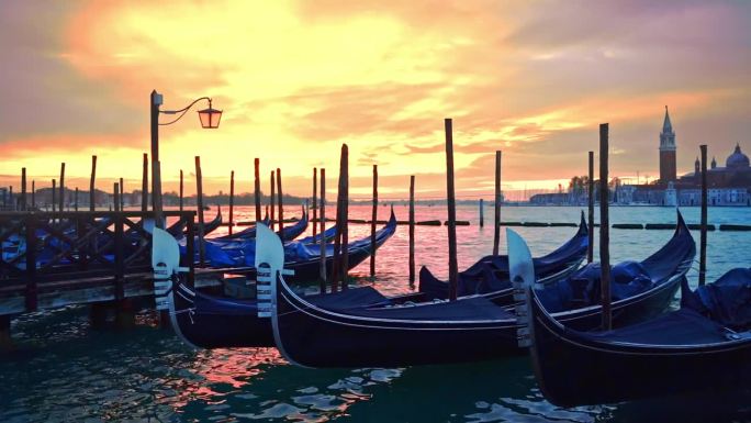 在威尼斯柔和的粉黄色日出中，摇曳的贡多拉和灯笼矗立在蔚蓝的泻湖中