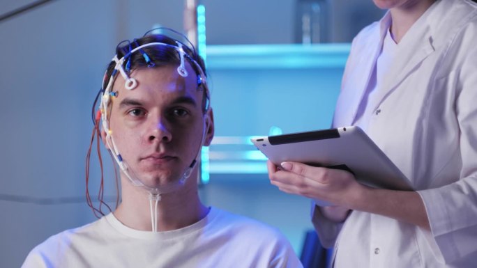 男子戴着脑电图拓形仪检查大脑，医生正在制作头皮活动电图。脑电图耳机对大脑工作的研究。