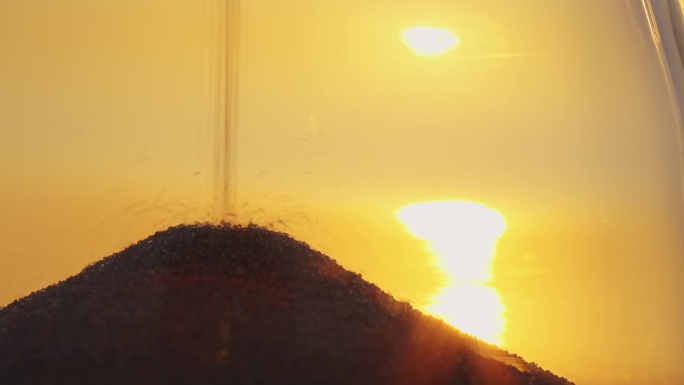时间概念沙漏特写在模糊的背景上的金色日落太阳盘在地平线上的天空在日落光线在夏季特写。金沙如流