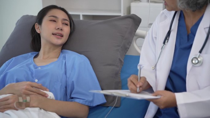 资深亚洲女医生在诊所辅导躺在病床上的年轻亚洲女性，在平板电脑4k 60p上讨论检查结果、健康建议或在