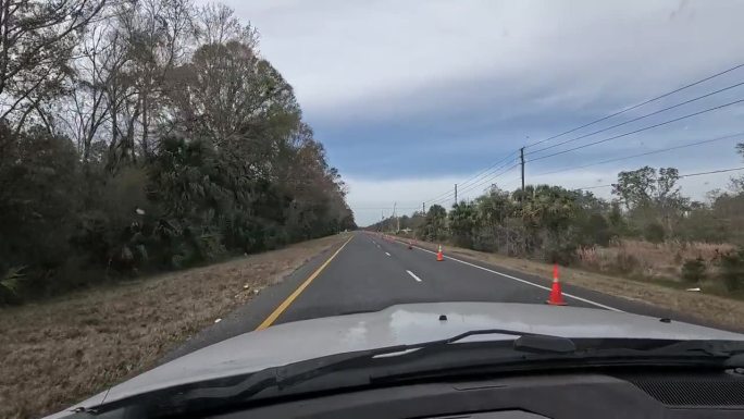 驾驶员在空旷的公路上行驶时的景象，道路施工橙色锥形锥体将交通合并成一条车道