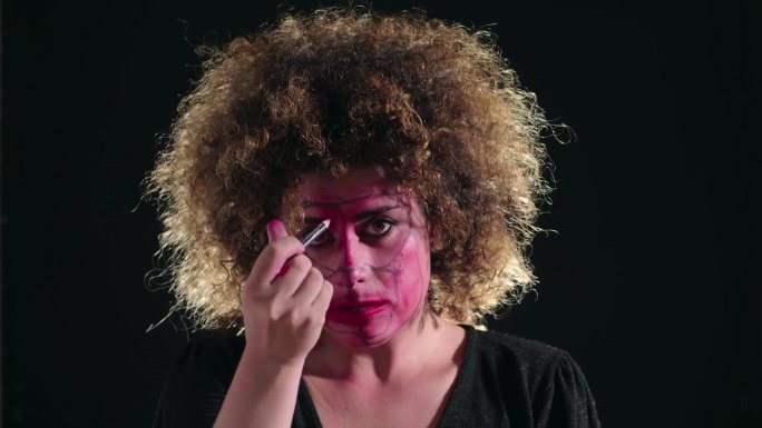 一个精神失常的女人在镜头前用眼线笔画着自己的脸