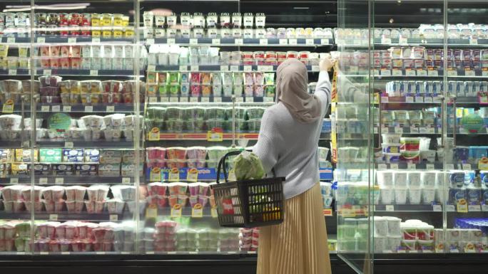 穆斯林妇女从超市的冷藏柜里购买食品的后视图