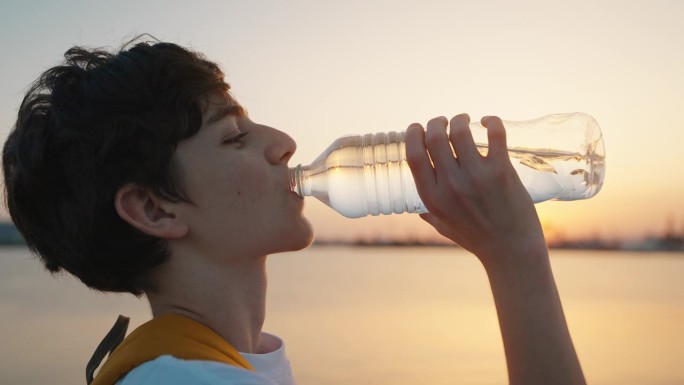 男性青少年热时贪喝瓶子里的水暑假运动或运动日落后骑自行车散步后不正常的热。白种人男孩在大热天喝矿泉水