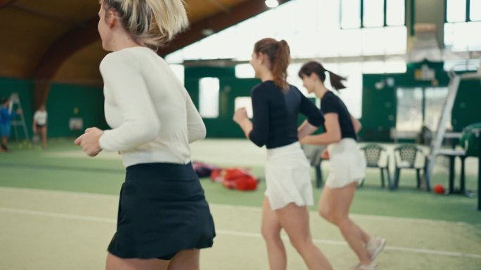 体育俱乐部网球场上，穿着运动服的运动女青年正在做热身运动