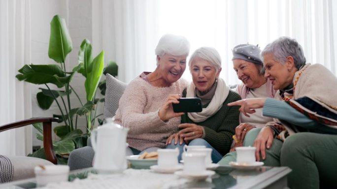 手机、自拍和老年女性朋友在家里的客厅一起参加茶话会。微笑着，退休和一群老人一起坐在沙发上一边拍照