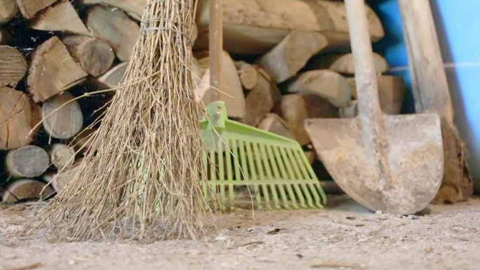 园林工具如树枝扫帚，耙子和铲子在仓库附近的房子，伐木背景上的园林设备，园丁和农民的工作工具的概念