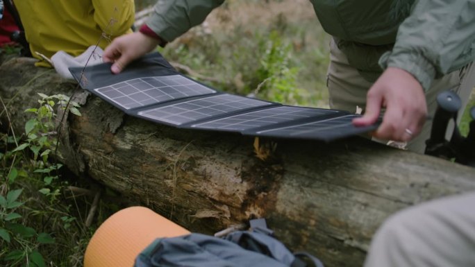 旅行者将太阳能电池板放在躺着的原木上，为设备充电