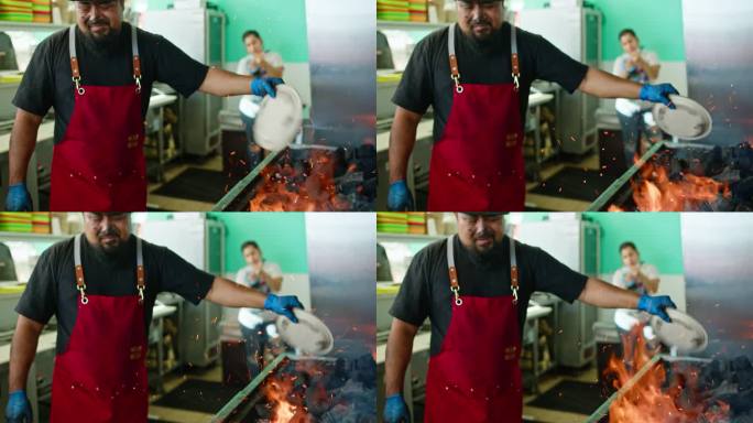 男厨师在煤盖烤架上扇火的中景