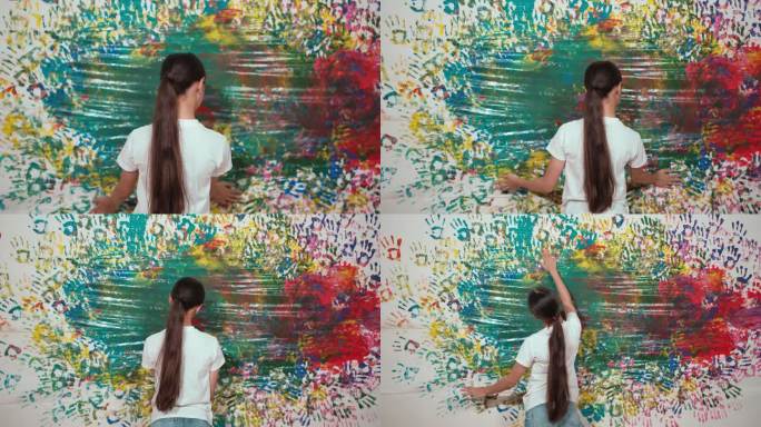 可爱女孩的后视图，用彩色的手涂满了污迹斑斑的墙壁。启迪