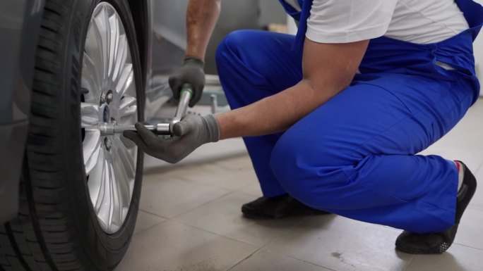 在现代汽车修理厂，穿蓝色制服的汽车技工用扭矩扳手拧紧汽车的合金车轮。熟练的技师确保豪华车的安全、精密