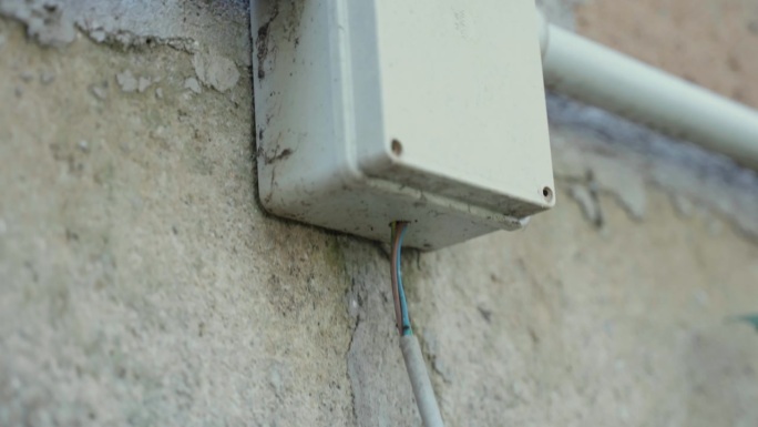 脏塑料电源箱，箱体上挂红蓝电缆接电，外墙上安装插座，接线连接，电源延伸概念