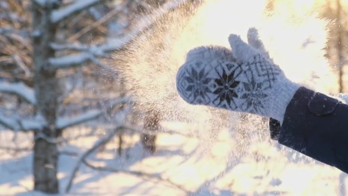 冬季公园里，戴着连指手套的女性拍手，玩雪。特写，超级慢镜头。在夕阳和阳光的映衬下，雪花飞扬。在阳光明