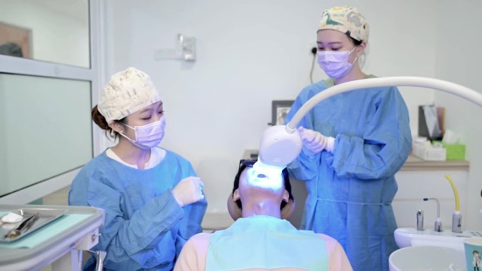 亚裔华裔女牙医正在为她的病人美白牙齿。