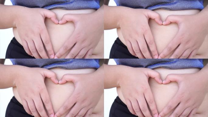 胖女人露出心形的手放在肚子上，为身体护理，怀孕饮食。亚洲年轻女性在暴饮暴食中存在肥胖问题。4 k