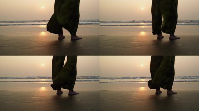 日落时分，女性的脚光着脚站在海边。黄昏时，女人站在海边，宽大的裤子随风飘动。自由和放松的概念。