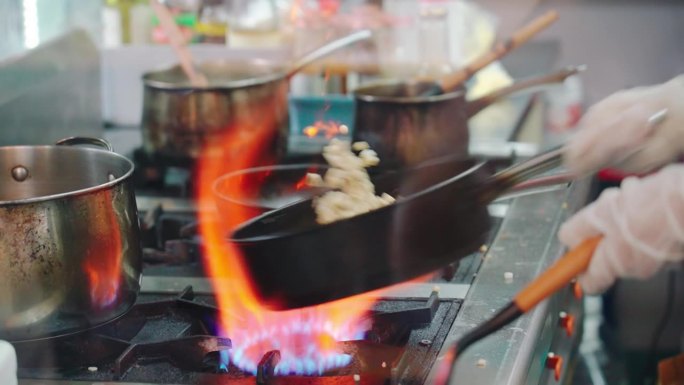 专业厨师在厨房用燃烧的煤气在平底锅上烹饪食物