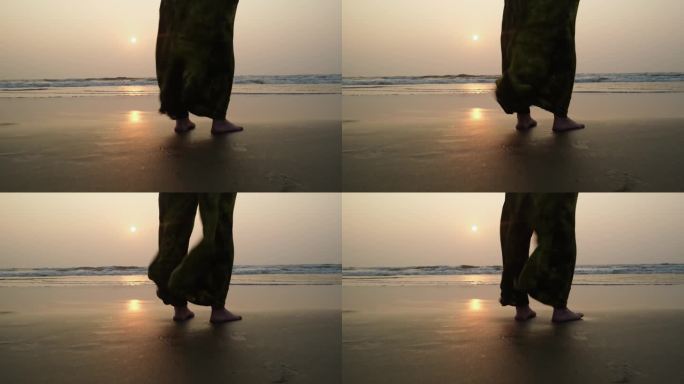 日落时分，女性的脚光着脚站在海边。黄昏时，女人站在海边，宽大的裤子随风飘动。自由和放松的概念。
