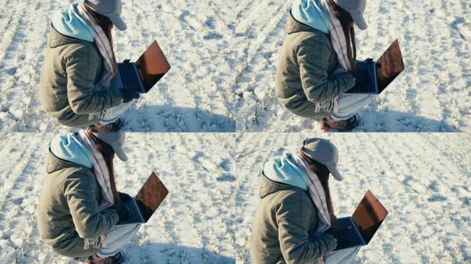 蹲伏在雪地上，穿着保暖衣服的女农学家用手提电脑的高视角