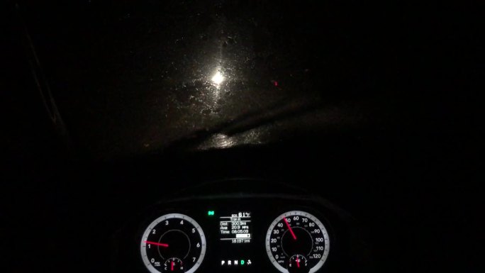 夜间驾驶员在多雨的乡村山路上行驶的景象，仪表盘清晰可见，迎面而来的车辆前灯阻碍了能见度