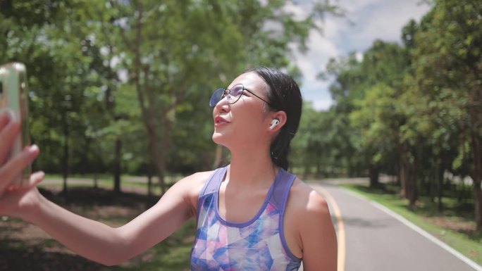 运动女性网红一边在公园慢跑锻炼，一边用智能手机录制视频博客直播，上传到社交媒体