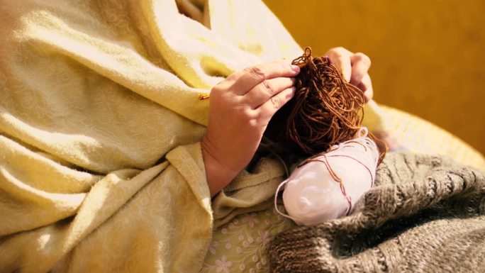 一个女人织羊毛围巾的特写镜头。一位女士用粗纱缝纫。
