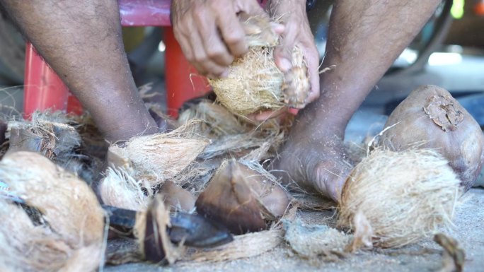 亚洲人用腿和工具剥椰子。