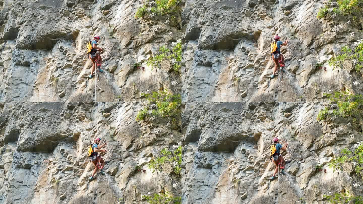 男攀登者用凿岩机和旋锤在攀绳上开辟一条新的攀登路线。登山者戴着红色头盔，背着黄色背包。