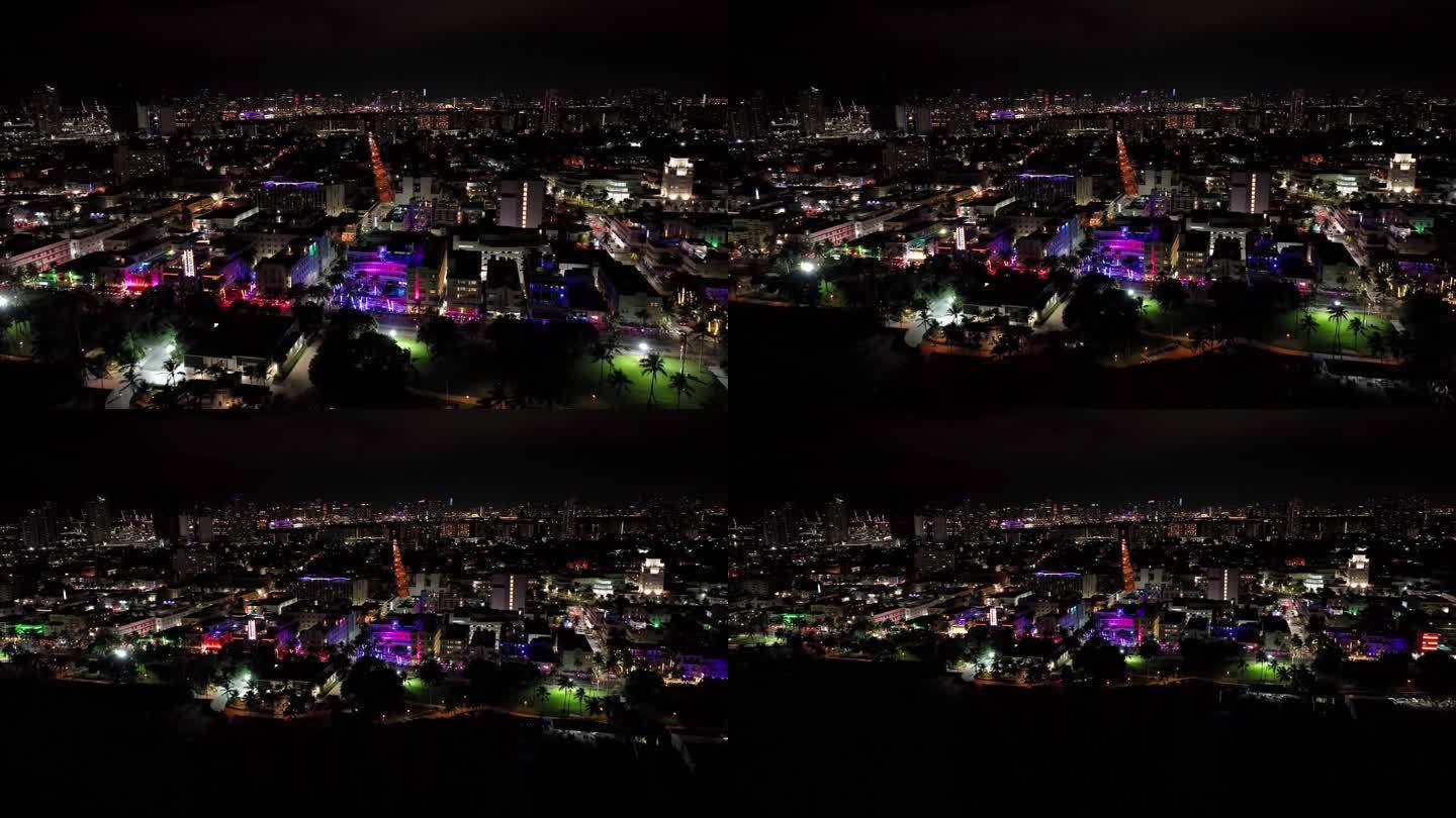暗示性的美国迈阿密夜间无人机镜头:缓慢的向后移动，从城市的建筑物、彩色灯光、道路，到海边和黑暗的大海