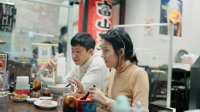 两个年轻的亚洲朋友一边聊天，一边喝着拉面汤，一边享受着桌上的日本面条