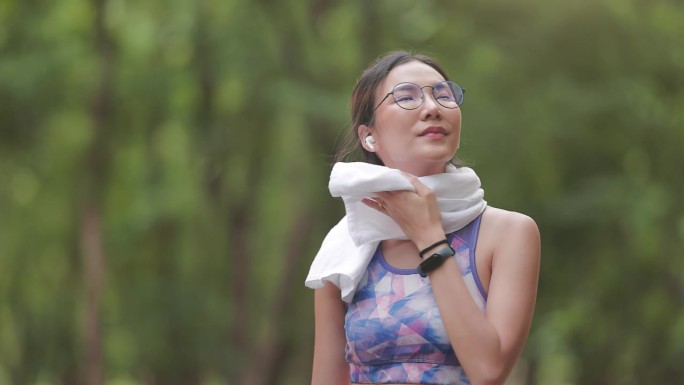 一位亚洲妇女在公园慢跑时用毛巾擦拭脸上的汗水。