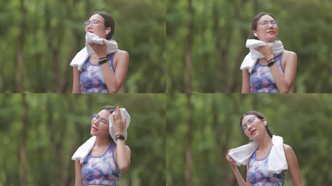一位亚洲妇女在公园慢跑时用毛巾擦拭脸上的汗水。