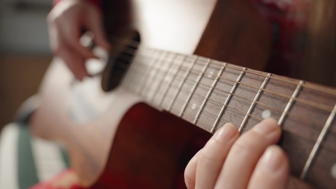 女性的手在阳光下弹吉他，用快速快门相机拍摄的琴弦振动特写。