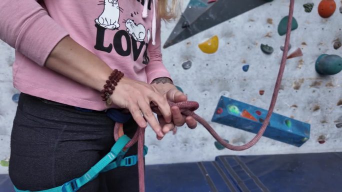 女攀岩者在攀岩墙前用绳结技术系好攀岩绳，为安全攀登做准备。