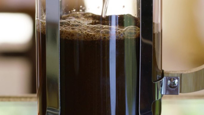 在一个玻璃壶里，滚烫的水倒在棕色的碎咖啡上。