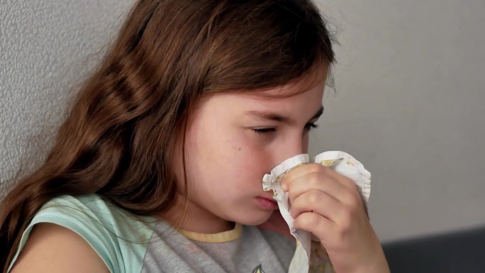 一个流着鼻涕的9岁小女孩坐在床上，头发蓬乱。他用手帕擤鼻涕