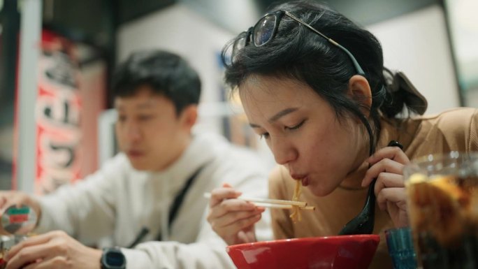 幸福的亚洲夫妇用筷子夹方便面和吃热日本拉面在日本餐馆