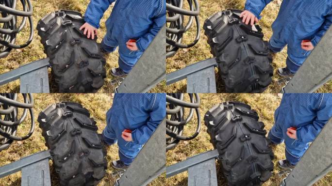 一个小男孩旋转着他父亲四轮摩托车的齿形轮胎。他扮演汽车修理工。雪炮有轮子，可以运送到滑雪区的下一个斜