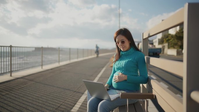 一位亚洲孕妇在海滩边使用笔记本电脑