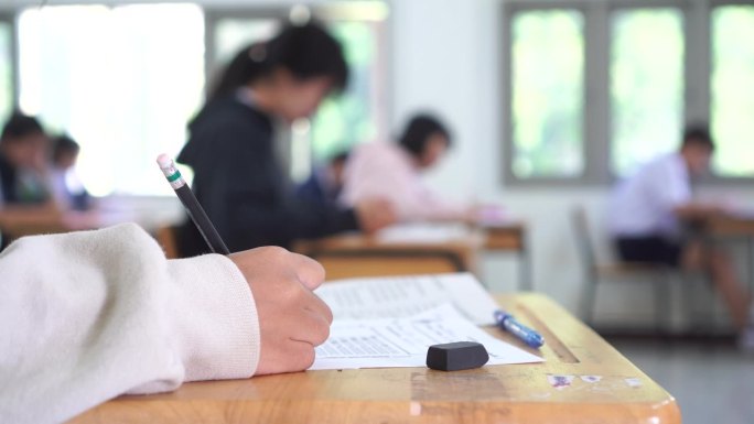 亚洲学生在课堂上使用橡皮擦书写学习考试。在高中的教育。学校学生的阅读笔记，评估在同学入学答卷上的写作