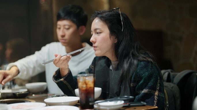 一名亚洲男子和一名女子在日本烧肉餐厅用传统的木炭烤架做饭和吃肉。