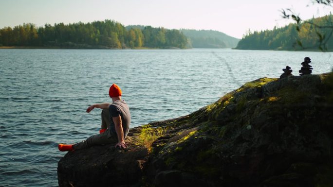 独自去大自然旅行，年轻的成年男子坐在湖边的石头上观看自然景观
