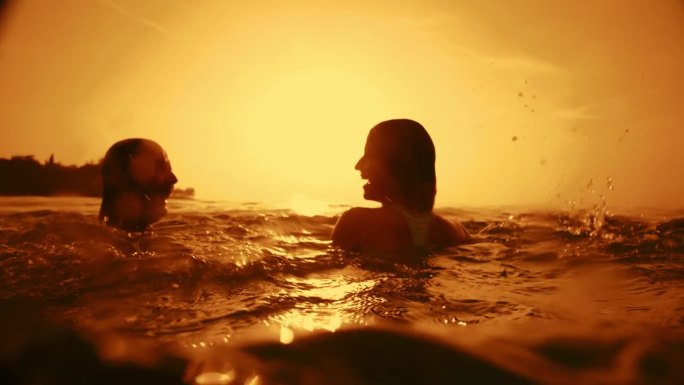 夕阳下，一对无忧无虑的夫妇张开双臂在宁静的海水中游泳