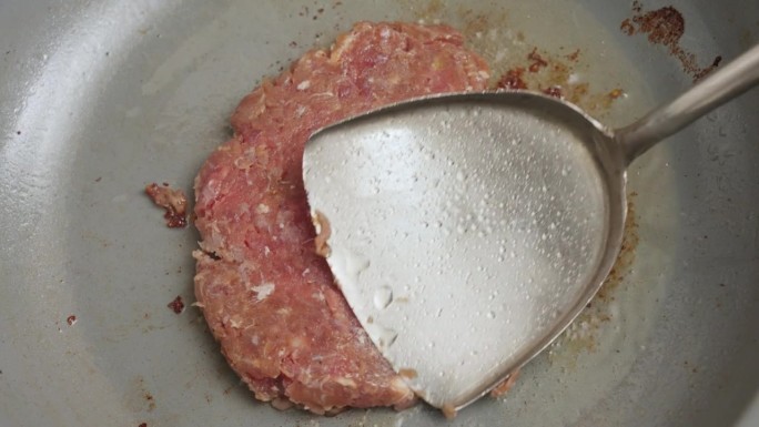 用锅铲在煎锅里煎汉堡肉饼。