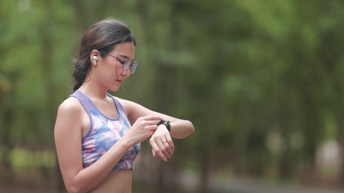 年轻女子在户外慢跑，用她的智能手表检查心率区，以便在公园进行晨间训练