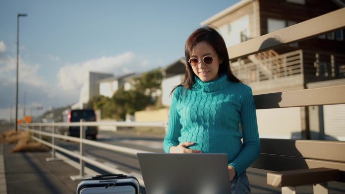 亚洲女性一边用笔记本电脑工作，一边欣赏美丽的海滨景色